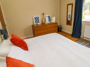A bedroom with a bed with orange pillows a wooden dresser with decorations and a mirror on the wall at Glynderi in Cilgerran