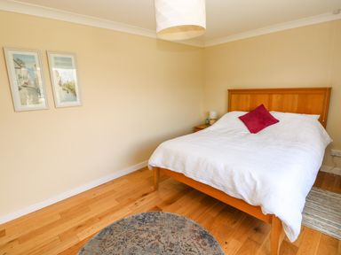 A bedroom with a wooden bed with white bedding and a red pillow with two paintings on the wall at Glynderi in Cilgerran