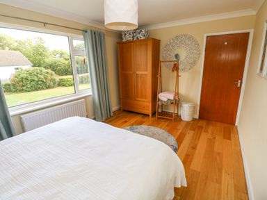 A bedroom with a bed next to a window with curtains a wooden wardrobe a coat rack and a round mirror on the wall at Glynderi in Cilgerran