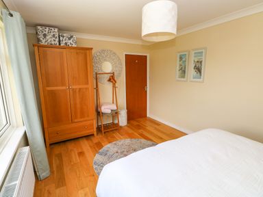 A bedroom with a wooden wardrobe a standing clothes rack a round rug and a bed with a white cover at Glynderi in Cilgerran