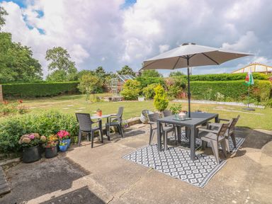 A garden patio with outdoor dining tables chairs and umbrella near plants and a greenhouse at Glynderi in Cilgerran