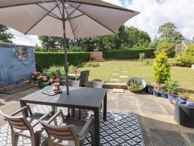 An outdoor patio with a table and chairs under an umbrella a garden shed and plants in pots at Glynderi in Cilgerran