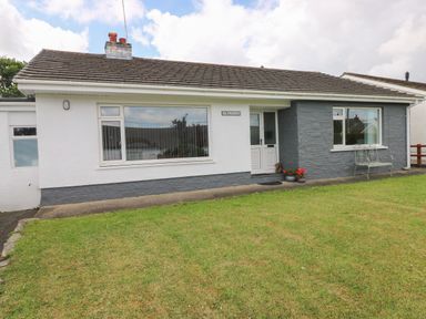A single story house with white and grey exterior walls front door and windows with a lawn at Glynderi in Cilgerran