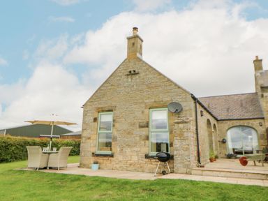 An outdoor patio area with table chairs and umbrella next to a stone house at The Byre in Longwitton near Morpeth