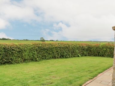 A grass lawn bordered by a hedge with a stone paved pathway at The Byre in Longwitton near Morpeth