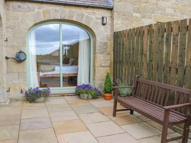 A patio area with a wooden bench plants and a large arched window at The Byre Longwitton near Morpeth