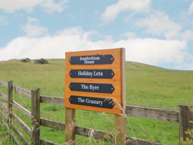 A wooden signpost with directions to Southwitton House Holiday Lets The Byre and The Granary in a grassy field