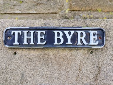 A metal sign with the words THE BYRE on a stone wall at The Byre in Longwitton near Morpeth