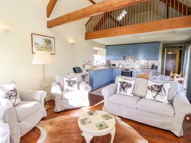 A living room with armchairs and sofa near a round coffee table and a kitchen with blue cabinets at The Byre Longwitton near Morpeth
