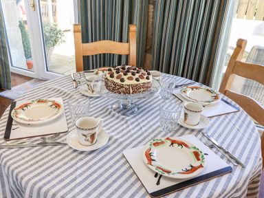 A dining table with a striped tablecloth set with animal themed plates cups and a cake on a glass stand at The Byre Longwitton near Morpeth