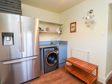 A utility room with refrigerator washing machine sink wooden bench and shelves at The Byre in Longwitton near Morpeth