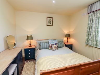 A bedroom with a wooden bed a dresser with a mirror and two bedside tables with lamps at The Byre in Longwitton near Morpeth