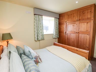 A bedroom with a wooden bed and wardrobe with patterned curtains on a window at The Byre in Longwitton near Morpeth