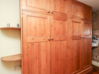 A wooden built-in wardrobe with paneled doors and round knobs next to curved wooden shelves at The Byre in Longwitton near Morpeth