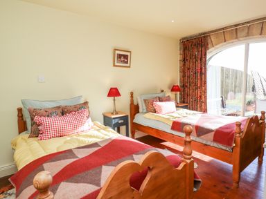 A bedroom with two single wooden beds bedside tables with red lamps and a large arched window at The Byre Longwitton near Morpeth
