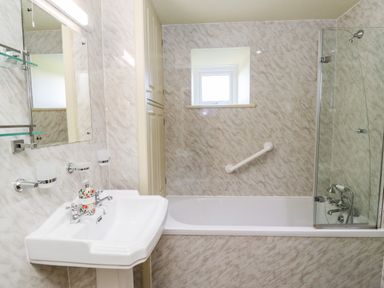 A bathroom with a pedestal sink a bathtub with a glass shower screen and a small window at The Byre in Longwitton near Morpeth