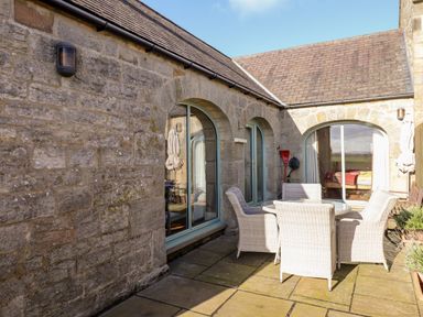 A stone patio with a round glass table and four wicker chairs at The Byre in Longwitton near Morpeth
