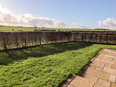 A lawn garden area next to a paved patio with a hedge fence and fields in the background at The Byre Longwitton near Morpeth