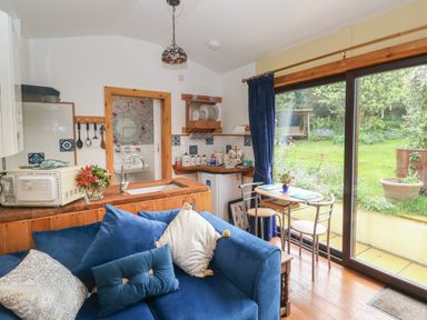 A small kitchen and dining area with a blue sofa and a glass sliding door opening to a garden at Turnpike Lodge in Brixham