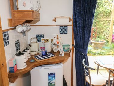 A kitchen corner with a kettle cups and jars on a wooden countertop next to a small fridge and blue curtain at Turnpike Lodge in Brixham