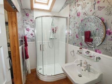 A bathroom with a glass shower enclosure a white sink and a round decorative mirror at Turnpike Lodge in Brixham