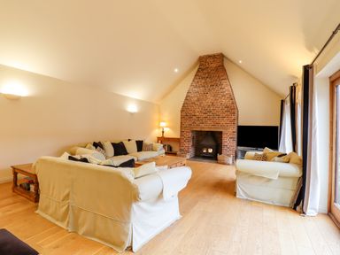 A living room with sofas around a wooden coffee table and a brick fireplace at The Stables at Hall Barn in Wattisfield near Walsham-Le-Willows
