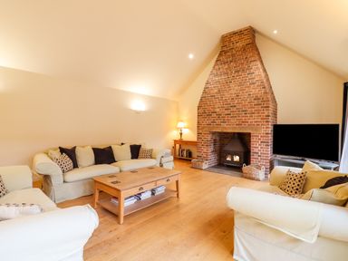 A living room with sofas a wooden coffee table a brick fireplace and a television at The Stables at Hall Barn in Wattisfield near Walsham-Le-Willows