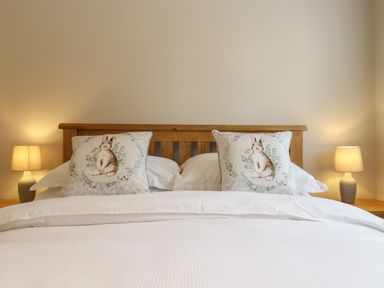A bedroom with a wooden bed frame white bedding pillows with rabbit designs and two bedside lamps at The Stables at Hall Barn in Wattisfield near Walsham-Le-Willows