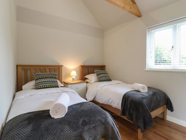 A bedroom with two single beds with wooden frames a bedside table with a lamp and window blinds at The Stables at Hall Barn Wattisfield near Walsham-Le-Willows