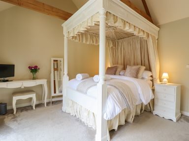 A bedroom with a four poster bed a bedside table with lamp and a desk with flowers at The Stables at Hall Barn Wattisfield near Walsham-Le-Willows