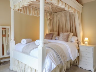 A bedroom with a four-poster bed pillows and rolled towels next to a bedside table with a lamp at The Stables at Hall Barn in Wattisfield near Walsham-Le-Willows