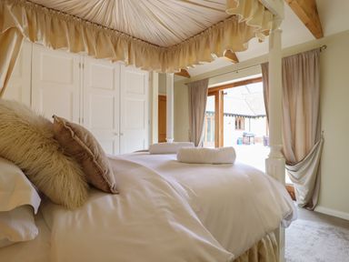 A bedroom with a canopy bed pillows and rolled towels near glass doors with curtains at The Stables at Hall Barn Wattisfield near Walsham-Le-Willows