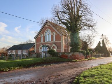 A building with a signboard and trees near a gravel road at The Stables at Hall Barn near Wattisfield near Walsham-Le-Willows