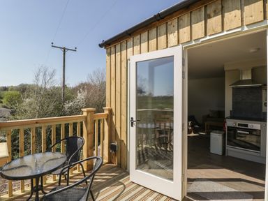 A balcony with a glass table and two chairs outside a kitchen with an open door at The Attic at Redmond Bottom in Wookey