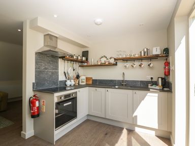 A kitchen with white cabinets and wooden shelves holding cups and plates at The Attic at Redmond Bottom in Wookey