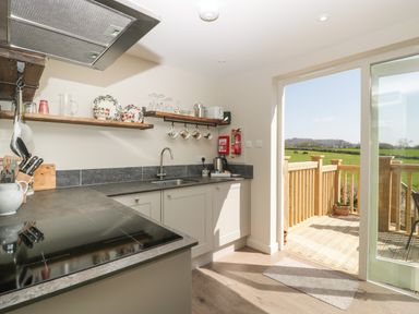 A kitchen with countertop stove open shelves and a door leading to a wooden deck with countryside view at The Attic at Redmond Bottom in Wookey