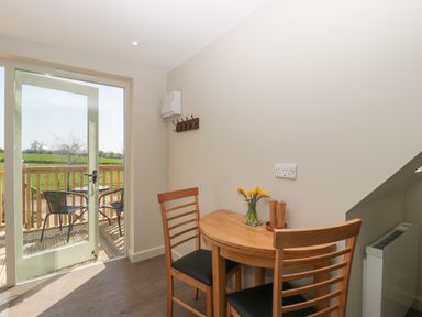 A small dining area with a wooden table and two chairs next to a glass door leading to a balcony with two chairs and a table at The Attic at Redmond Bottom in Wookey