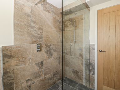 A shower area with stone tiles glass partition and a wooden door at The Attic at Redmond Bottom in Wookey