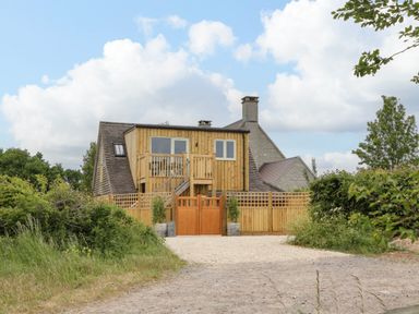 A wooden fenced house with a balcony and stairs surrounded by greenery and a gravel driveway at The Attic at Redmond Bottom in Wookey