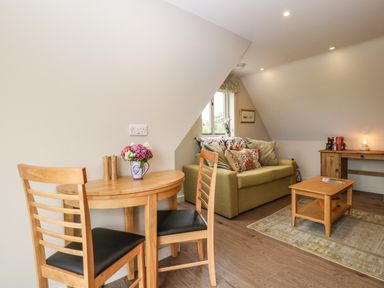 A small dining table with two chairs a green sofa with cushions a wooden coffee table and a wooden desk with a lamp at The Attic at Redmond Bottom in Wookey