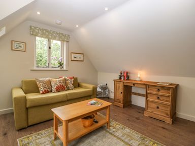 A living room with a green sofa pillows wooden coffee table and a wooden desk at The Attic at Redmond Bottom in Wookey