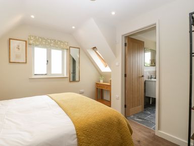 A bedroom with a bed covered by a yellow blanket a small wooden desk under a skylight window and a partially open door showing a bathroom at The Attic at Redmond Bottom in Wookey
