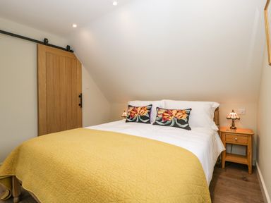 A bedroom with a bed covered with white sheets and a yellow quilt with floral pillows a wooden nightstand with a lamp and a wooden sliding door at The Attic at Redmond Bottom in Wookey