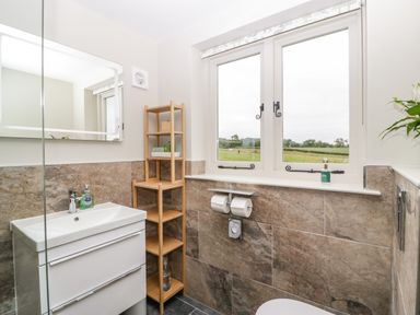 A bathroom with a sink, mirror, wooden shelves, toilet paper holder, and window showing a field at The Attic at Redmond Bottom in Wookey