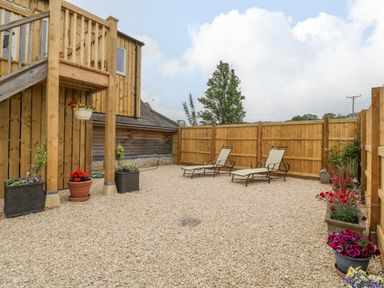 An outdoor patio area with two lounge chairs surrounded by wooden fences and potted plants at The Attic at Redmond Bottom in Wookey