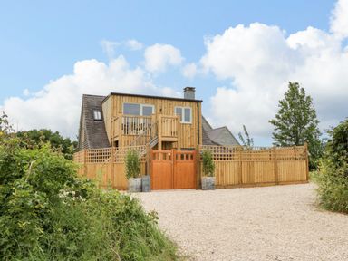 A wooden house with a fenced yard and gravel driveway at The Attic at Redmond Bottom in Wookey