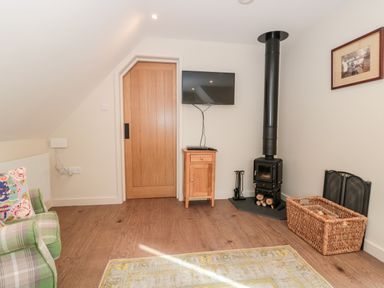 A sitting area with a green plaid armchair a wooden door a wall-mounted TV a wood-burning stove and a wicker basket at The Attic at Redmond Bottom in Wookey