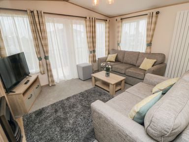 A living room with two sofas a coffee table a TV on a wooden stand a gray rug and curtains at 20 Wolds View East Heslerton near West Heslerton