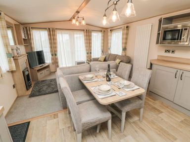 A dining table set for four adjacent to a living area with sofas a television and kitchen cabinets at 20 Wolds View in East Heslerton near West Heslerton