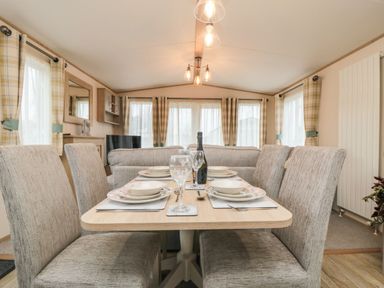 A dining area with a table set for four and armchairs in a living room with curtains on windows at 20 Wolds View East Heslerton near West Heslerton